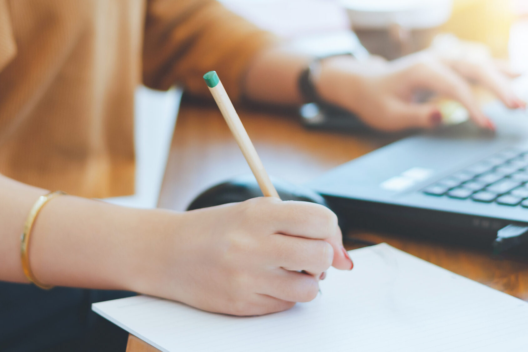 Closeup of hand asian businesswoman writing on paper and using laptop to searching data for working