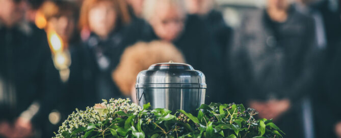A metal urn with ashes of a dead person on a funeral, with people mourning in the background on a memorial service. Sad grieving moment at the end of a life. Last farewell to a person in an urn.
